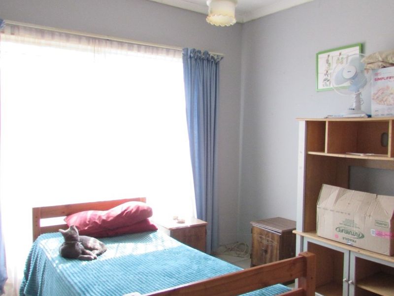 A functional bedroom featuring tiled flooring and a central pendant light fixture, with large window providing ample natural light.