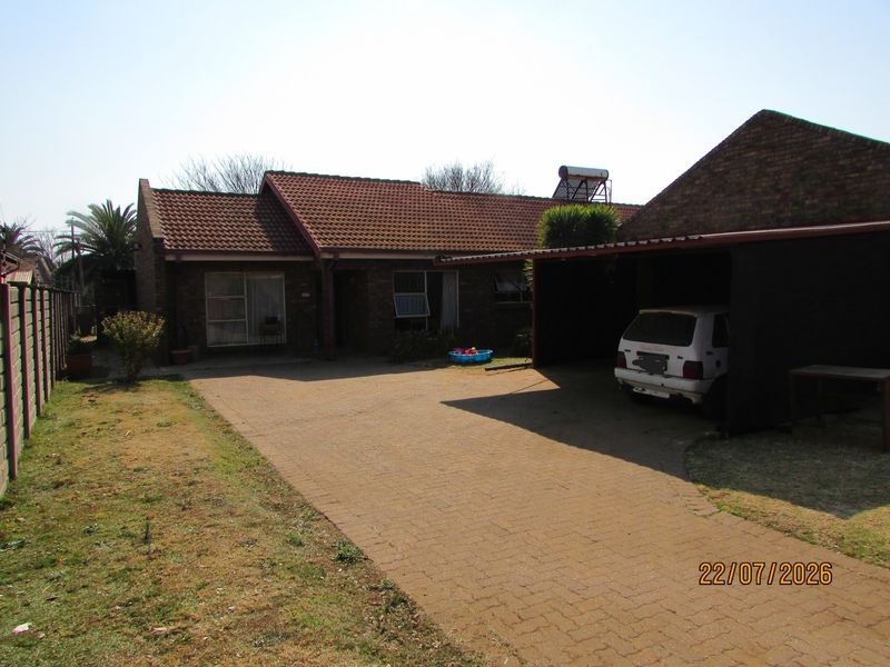 Front view of a brick house featuring a paved driveway, attached carport, and solar water heating system.