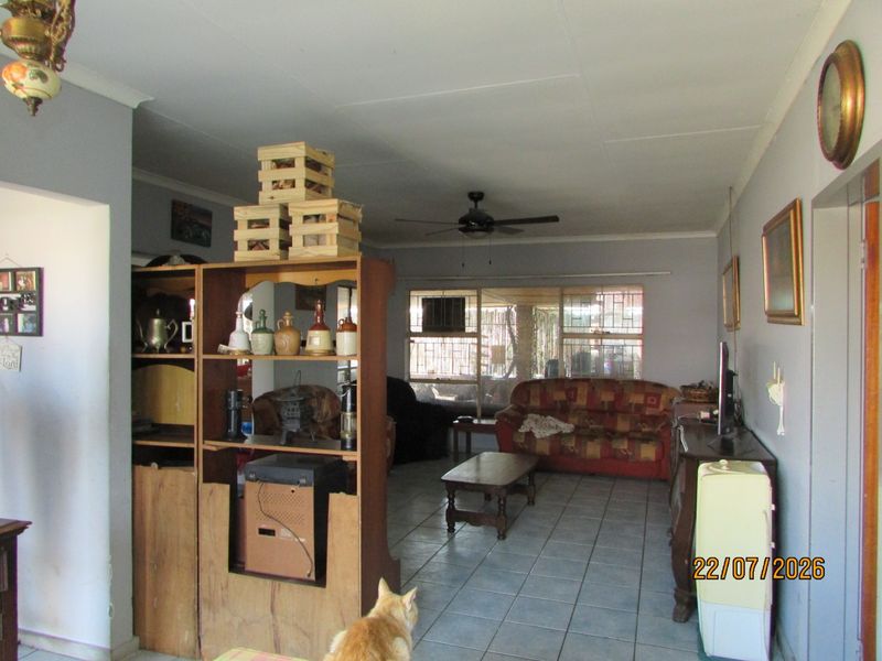 A spacious living room featuring tiled flooring, a ceiling fan, and large windows with security bars, offering a functional and well-lit living area.