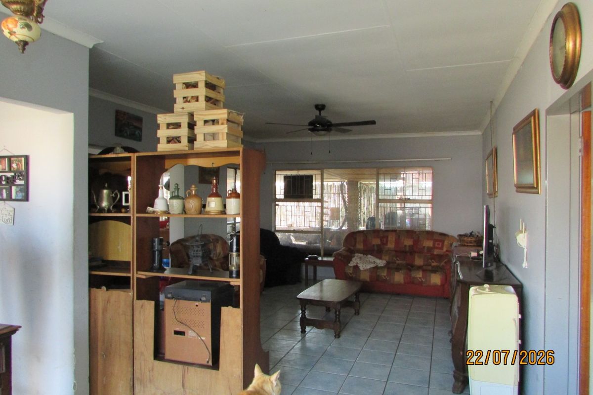 A spacious living room featuring tiled flooring, a ceiling fan, and large windows with security bars, offering a functional and well-lit living area.
