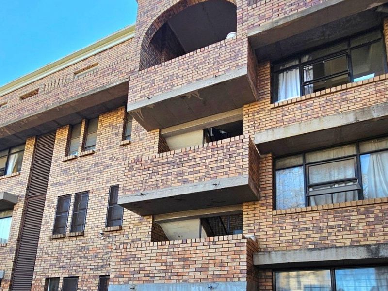 Exterior view of a multi-story commercial or residential building featuring face brick facade, concrete balconies, and steel-framed windows.