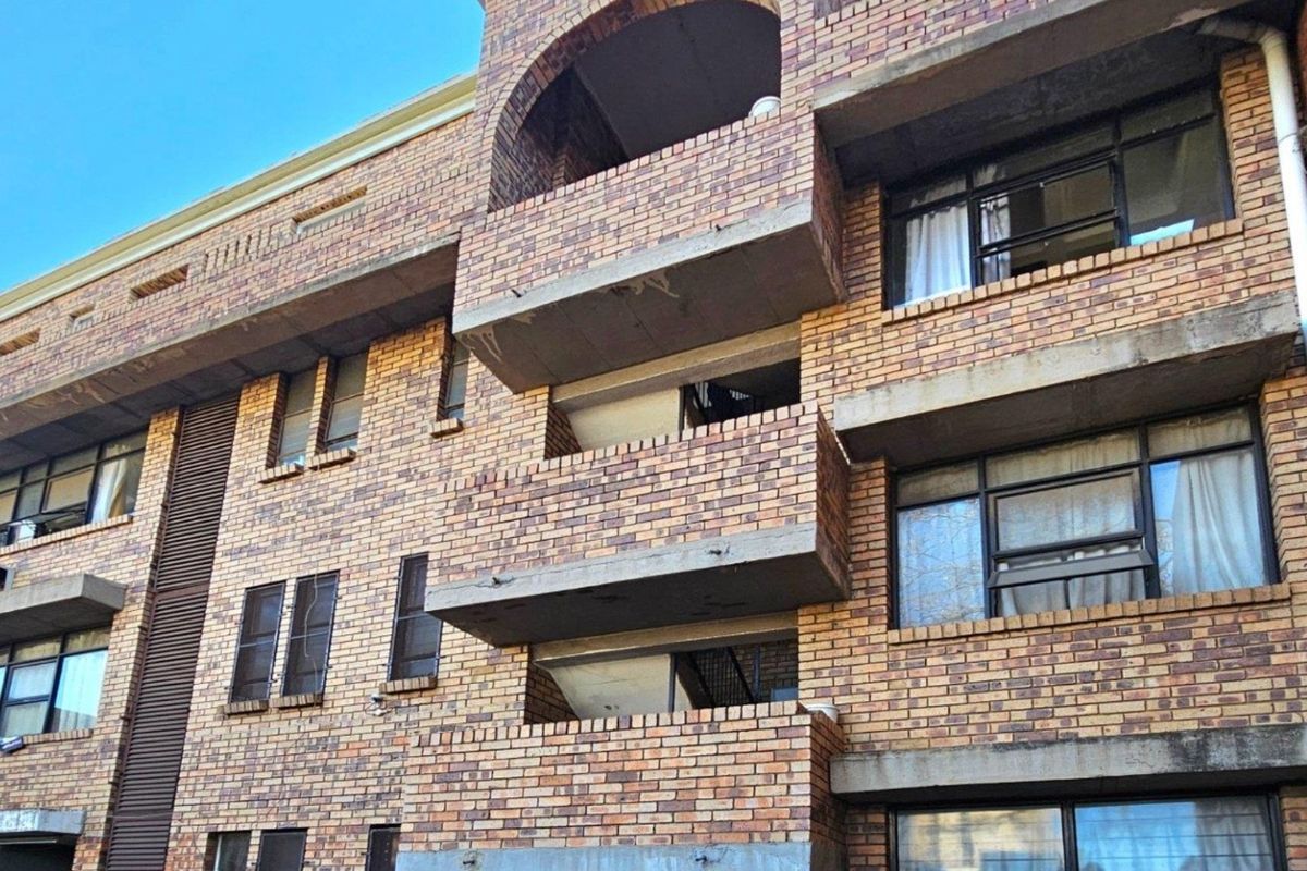 Exterior view of a multi-story commercial or residential building featuring face brick facade, concrete balconies, and steel-framed windows.