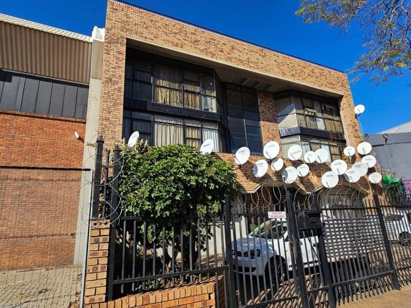 Front facade of a commercial brick building featuring extensive satellite dish installations, metal security fencing, and razor wire.