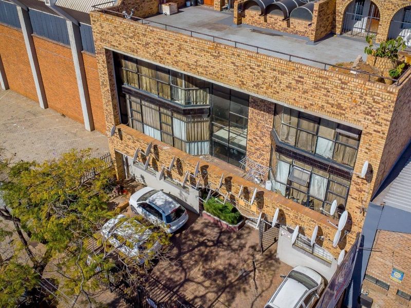 Aerial view of a multi-story commercial face brick building featuring a paved driveway, metal window frames, and a flat roof structure.