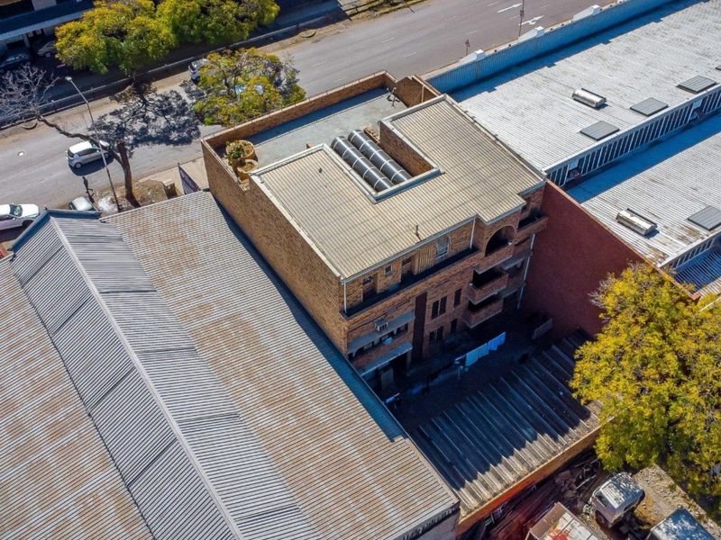 Aerial view of a multi-story commercial brick building featuring a metal roof with integrated skylights and multiple balconies.