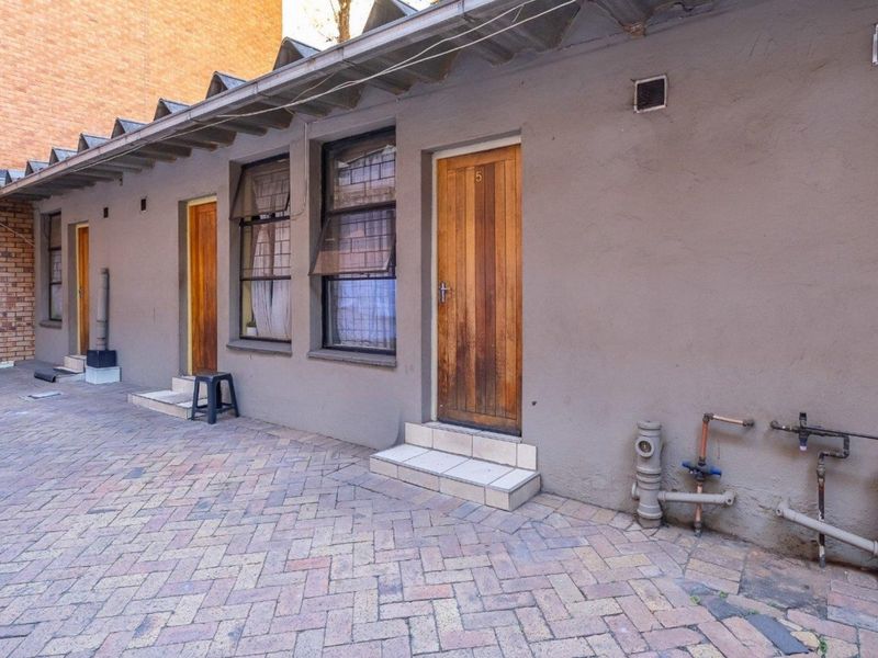 Rear exterior view of a commercial property featuring a paved courtyard, multiple timber access doors, and exposed external plumbing infrastructure.
