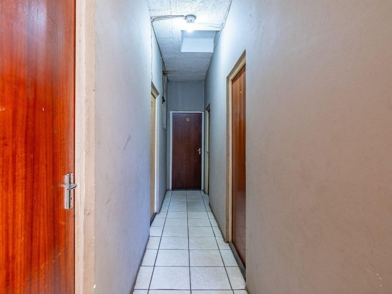 A narrow commercial hallway featuring tiled flooring and multiple wooden doors, showing signs of wear on the walls and ceiling.
