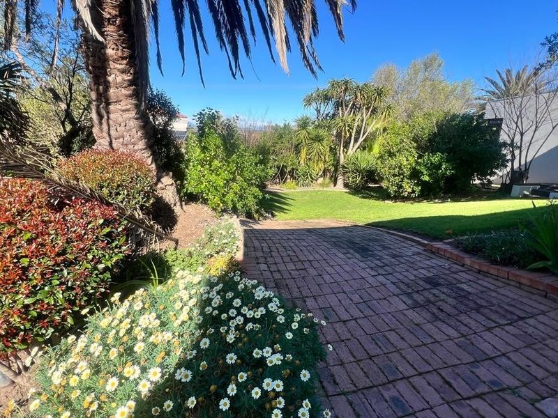 A well-maintained garden featuring a brick-paved pathway, lush green lawn, and mature landscaping, providing a serene outdoor space.