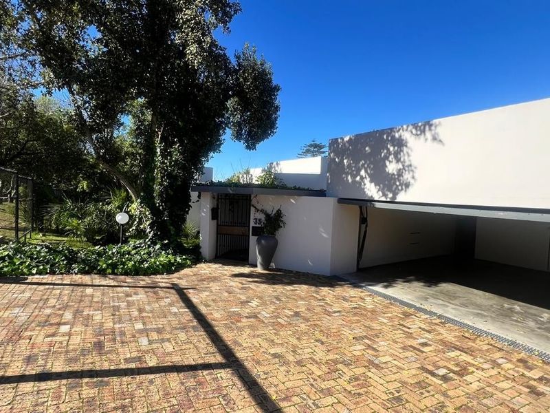 Front exterior view featuring a brick driveway, covered garage space, and secure gated entrance with established garden surroundings.
