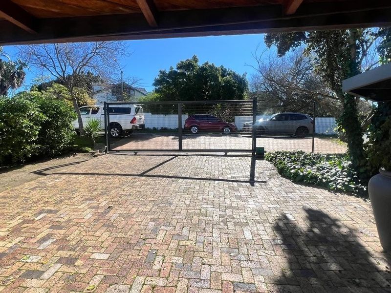 A paved driveway leading to a sliding security gate, providing access to the property with a covered entrance area.
