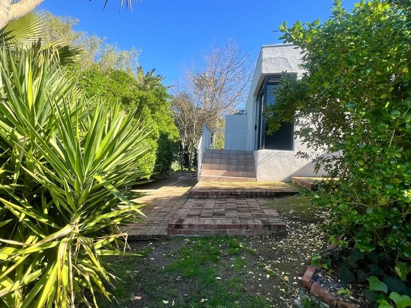 Rear garden area featuring brick paving, tiled steps leading to the building entrance, and established garden landscaping.