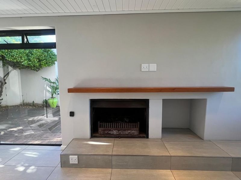 A bright living room featuring a built-in fireplace with a timber mantelpiece, tiled hearth, and large sliding glass doors leading to an outdoor area.