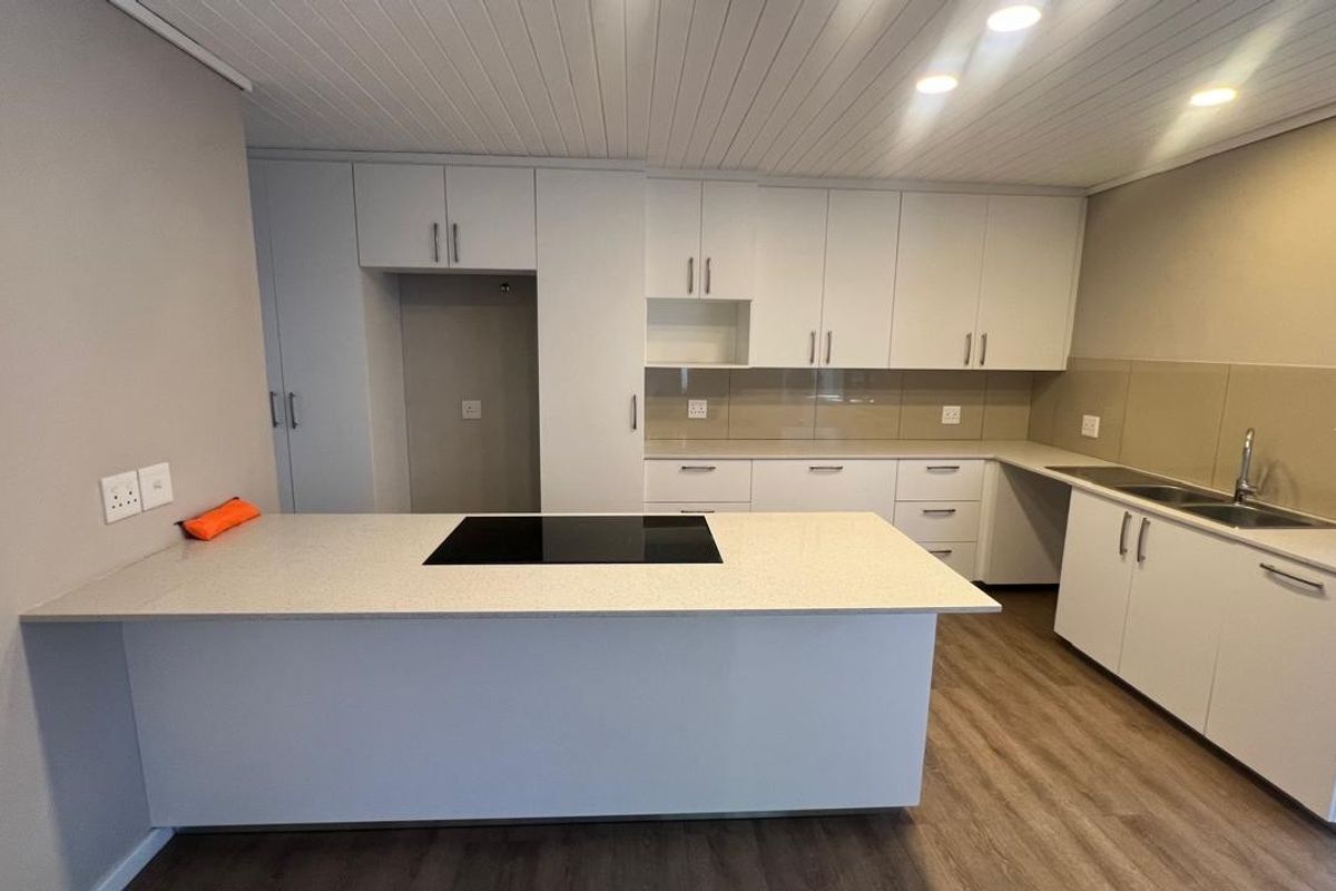 Modern kitchen featuring white cabinetry, stone countertops, an integrated induction hob, and a double sink with a glass splashback.