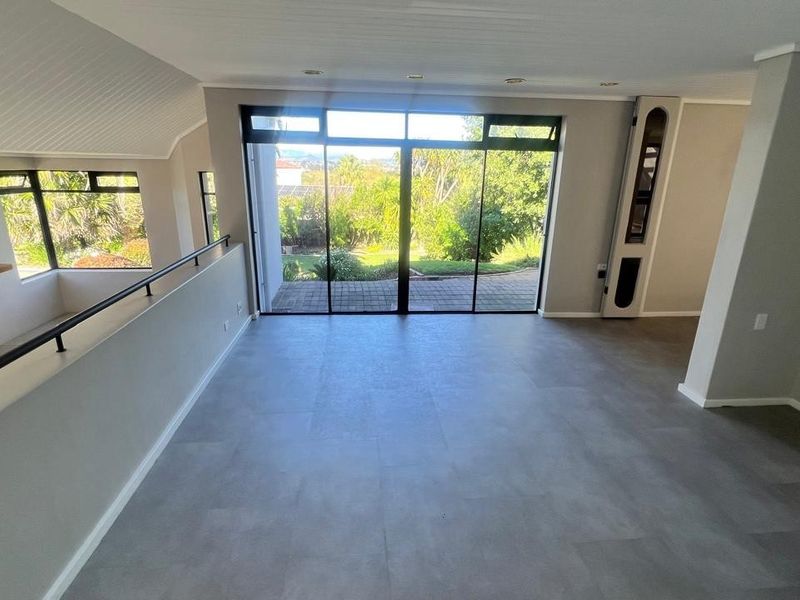 Spacious open-plan living area featuring large sliding glass doors, a fireplace, and neutral tiled flooring with views of the garden.