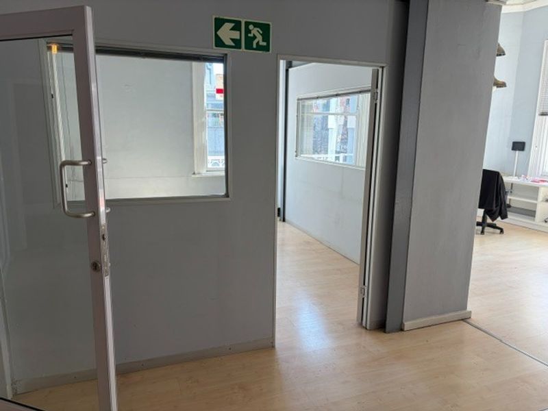 An empty office space featuring laminate flooring, glass partitions, and internal windows, providing a functional and bright professional work environment.