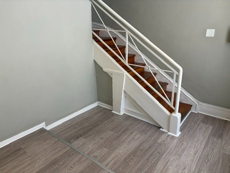 A clean, empty hallway featuring a wooden staircase with a white metal balustrade and modern laminate flooring.