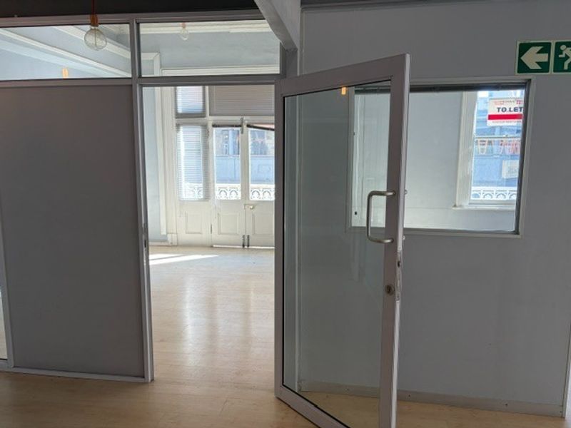 An empty office space featuring glass partitions, aluminum door frames, and light-toned laminate flooring, offering a bright and professional work environment.