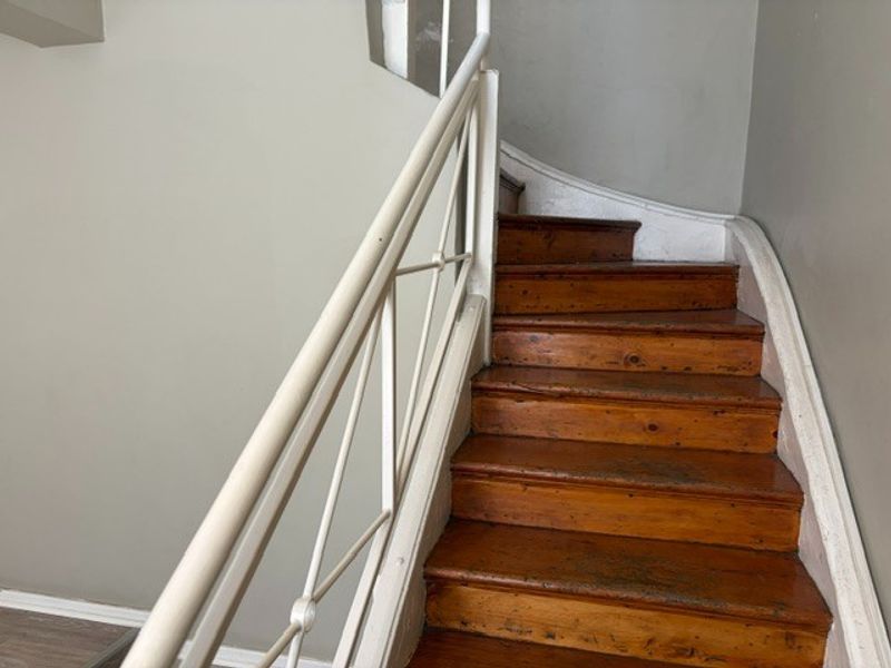 A functional wooden staircase with a metal handrail, showing signs of wear on the treads and surrounding wall finishes.