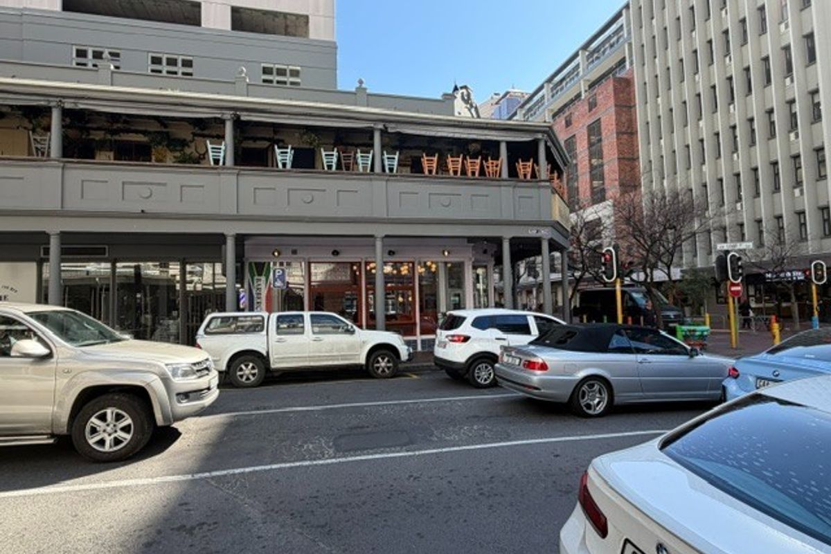 Street-level view of a commercial office building featuring a prominent covered balcony and ground-floor storefront access in a busy urban setting.