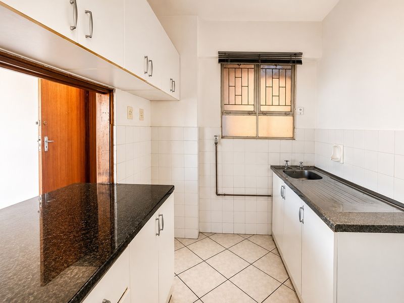 A functional kitchen featuring white cabinetry, dark granite countertops, tiled flooring, and a stainless steel sink with an exposed plumbing pipe.