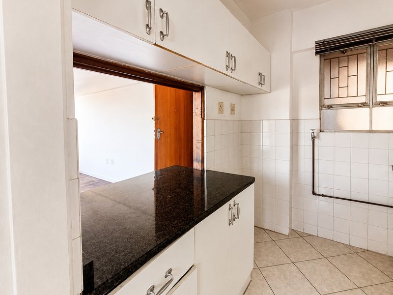 A functional kitchen featuring white cabinetry, dark granite countertops, tiled backsplash, and a convenient pass-through window connecting to the adjacent living area.