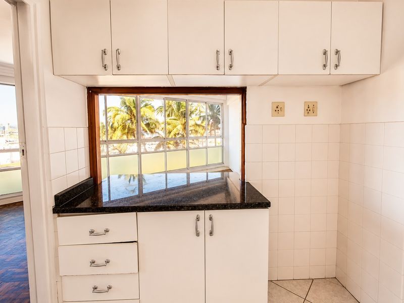 A compact kitchen area featuring white cabinetry, granite countertops, and a convenient pass-through window overlooking the exterior.