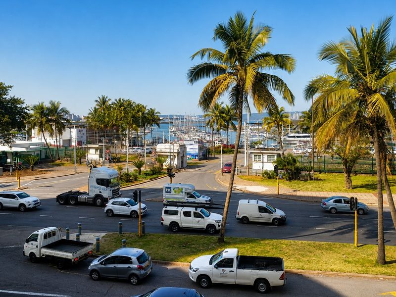 Elevated view overlooking a busy street intersection with palm trees and a marina in the background.
