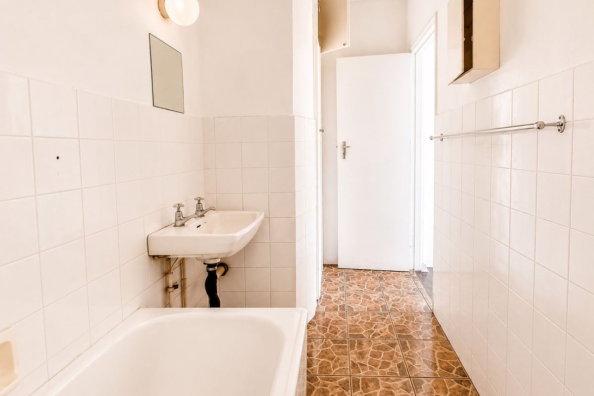 A functional bathroom featuring a wall-mounted basin, bathtub, and tiled finishes, offering a blank canvas for potential modernization and renovation.