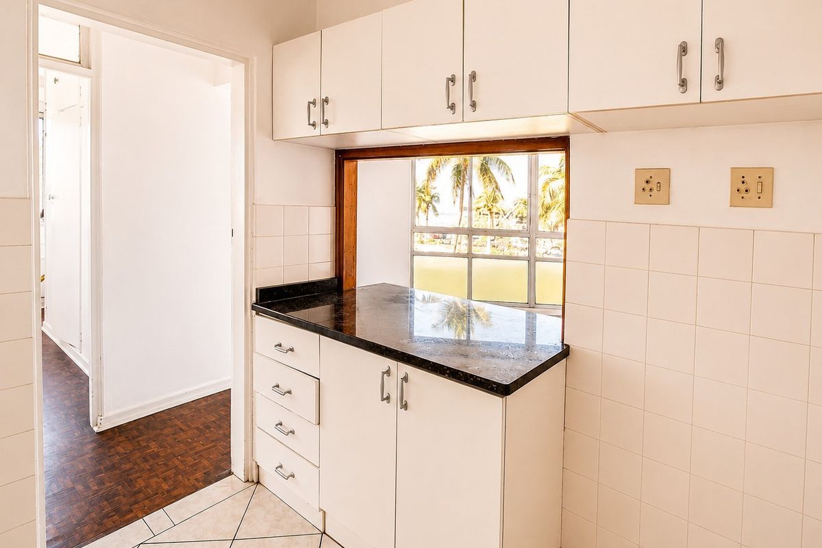 A functional kitchen area featuring white built-in cabinetry, dark granite countertops, and a convenient pass-through window with views.