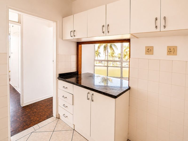 A functional kitchen area featuring white built-in cabinetry, dark granite countertops, and a convenient pass-through window with views.