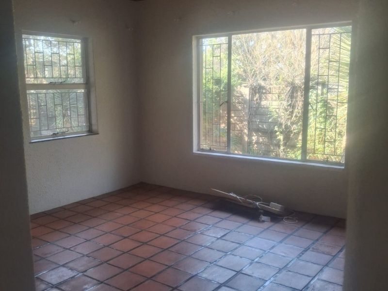 An empty living room featuring terracotta floor tiles, a timber-clad ceiling with a ceiling fan, and windows fitted with security bars.