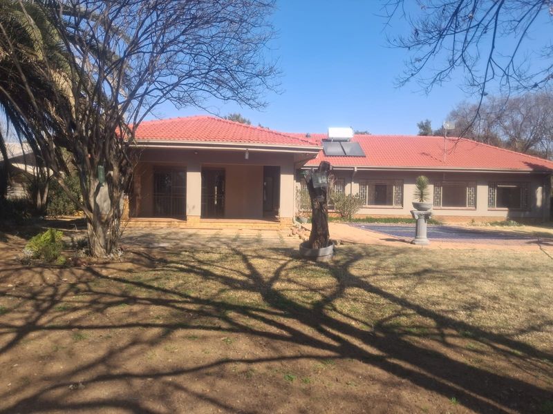 Rear view of the house featuring a tiled roof with solar water heating, a covered patio, and a swimming pool set in a garden.