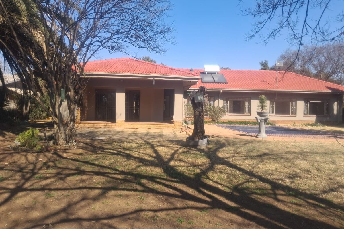 Rear view of the house featuring a tiled roof with solar water heating, a covered patio, and a swimming pool set in a garden.