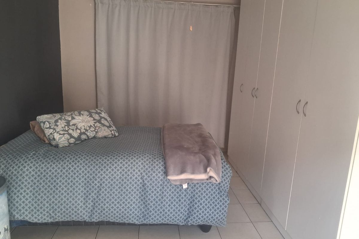 A functional bedroom featuring neutral tiled flooring and ample built-in cupboard storage space.