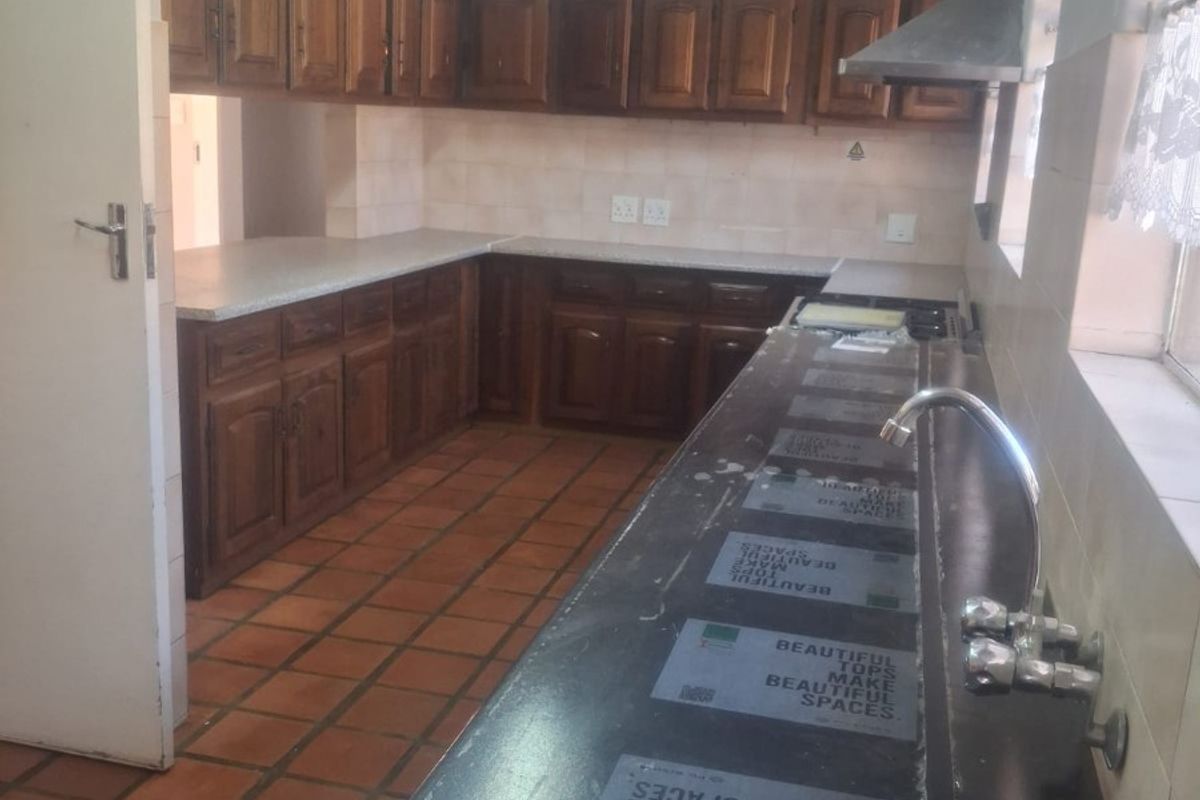 A functional kitchen featuring wooden cabinetry, laminate countertops, a stainless steel extractor fan, and tiled flooring, offering a classic layout ready for modernization.