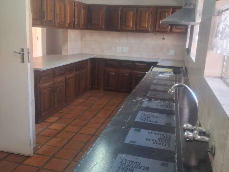 A functional kitchen featuring wooden cabinetry, laminate countertops, a stainless steel extractor fan, and tiled flooring, offering a classic layout ready for modernization.