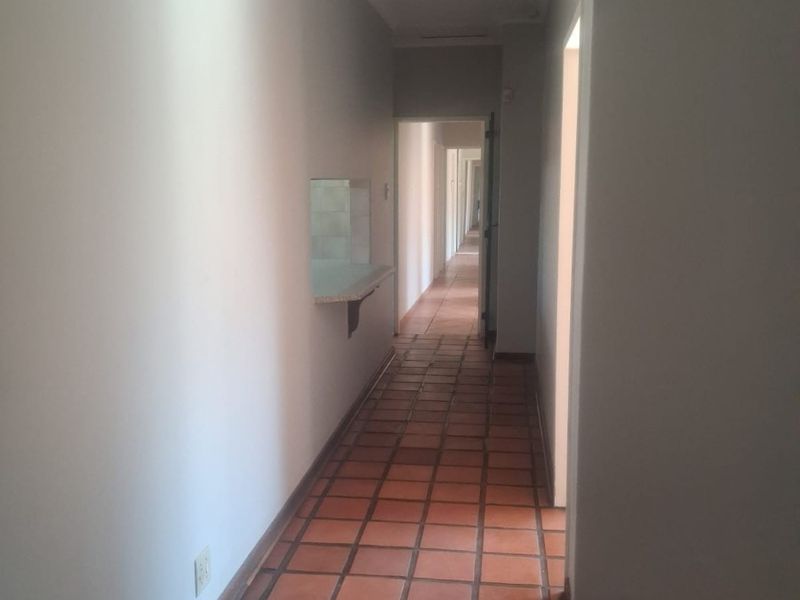 A long, empty hallway featuring terracotta tile flooring, recessed lighting, and a pass-through window opening into an adjacent room.