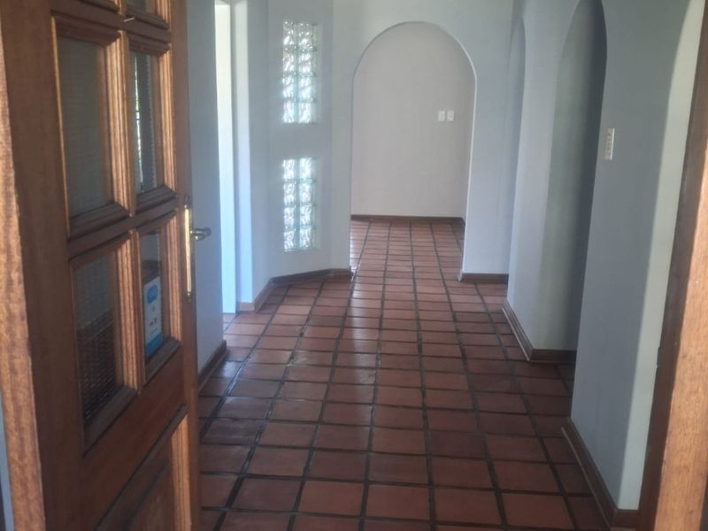 A bright entrance hallway featuring terracotta floor tiles, arched architectural details, and a unique glass block feature wall.