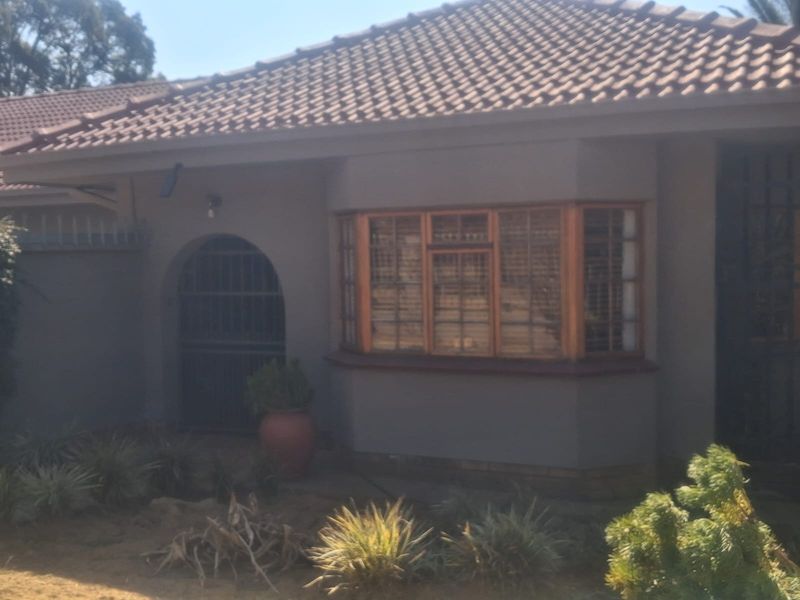 Front facade of the house featuring a tiled roof, a prominent bay window with wooden frames, and an arched entrance with a security gate.
