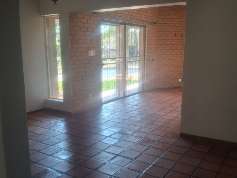 Spacious living area featuring terracotta floor tiles, exposed brick feature wall, and sliding glass doors leading to the outdoor area.