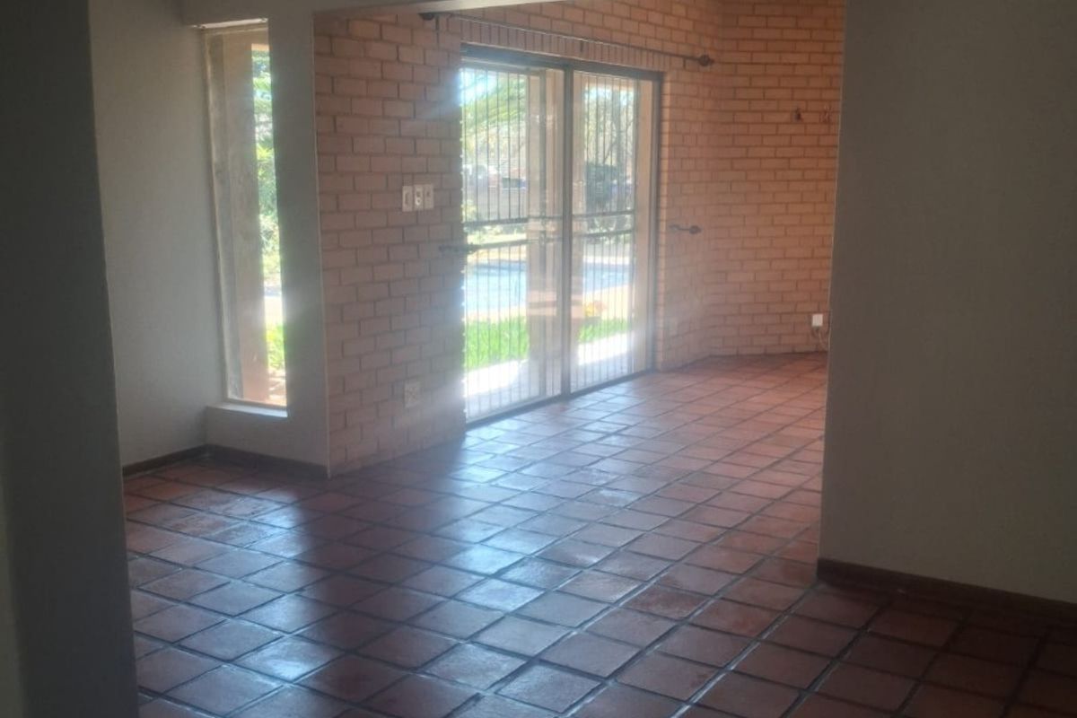 Spacious living area featuring terracotta floor tiles, exposed brick feature wall, and sliding glass doors leading to the outdoor area.