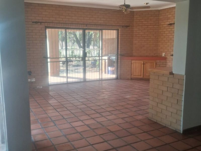 Spacious living area featuring terracotta floor tiles, exposed brick walls, a ceiling fan, and a sliding glass door leading to the outdoor space.