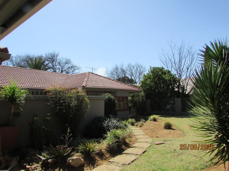 A view of the rear garden featuring a tiled roof house, established landscaping, and a stone pathway leading through the yard.