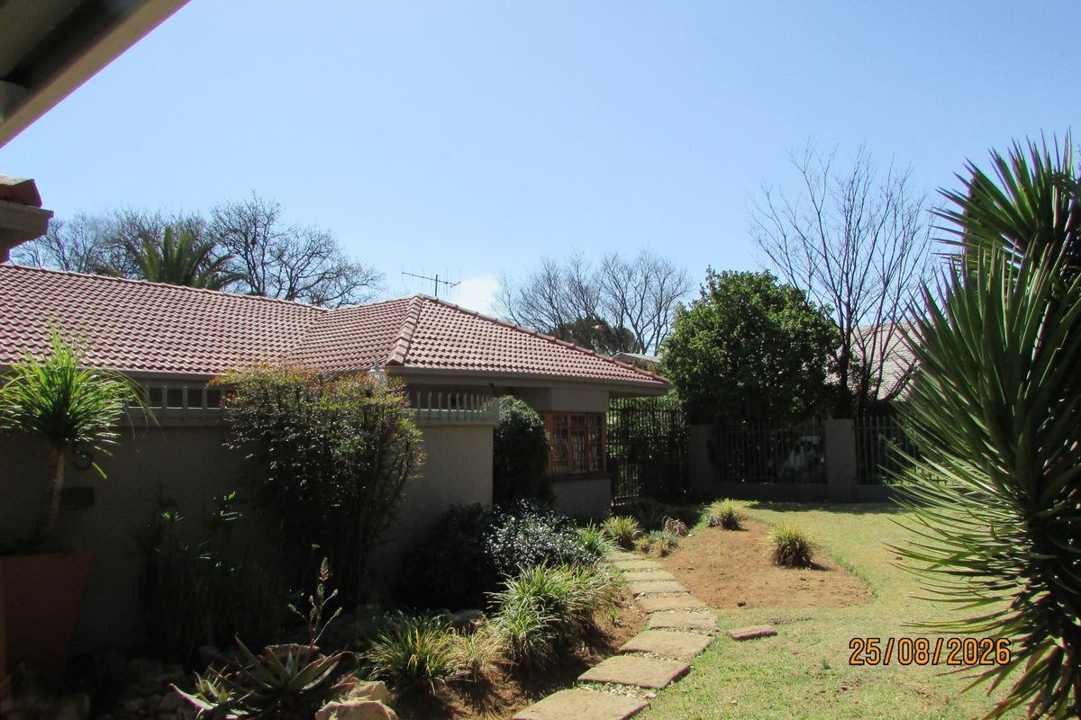 A view of the rear garden featuring a tiled roof house, established landscaping, and a stone pathway leading through the yard.