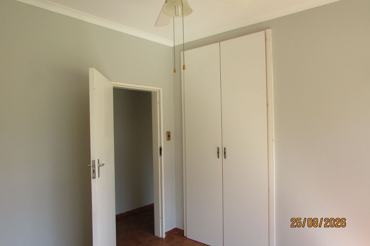 A clean, empty bedroom featuring built-in wardrobes, a ceiling fan, and tiled flooring, offering a neutral canvas for personalization.