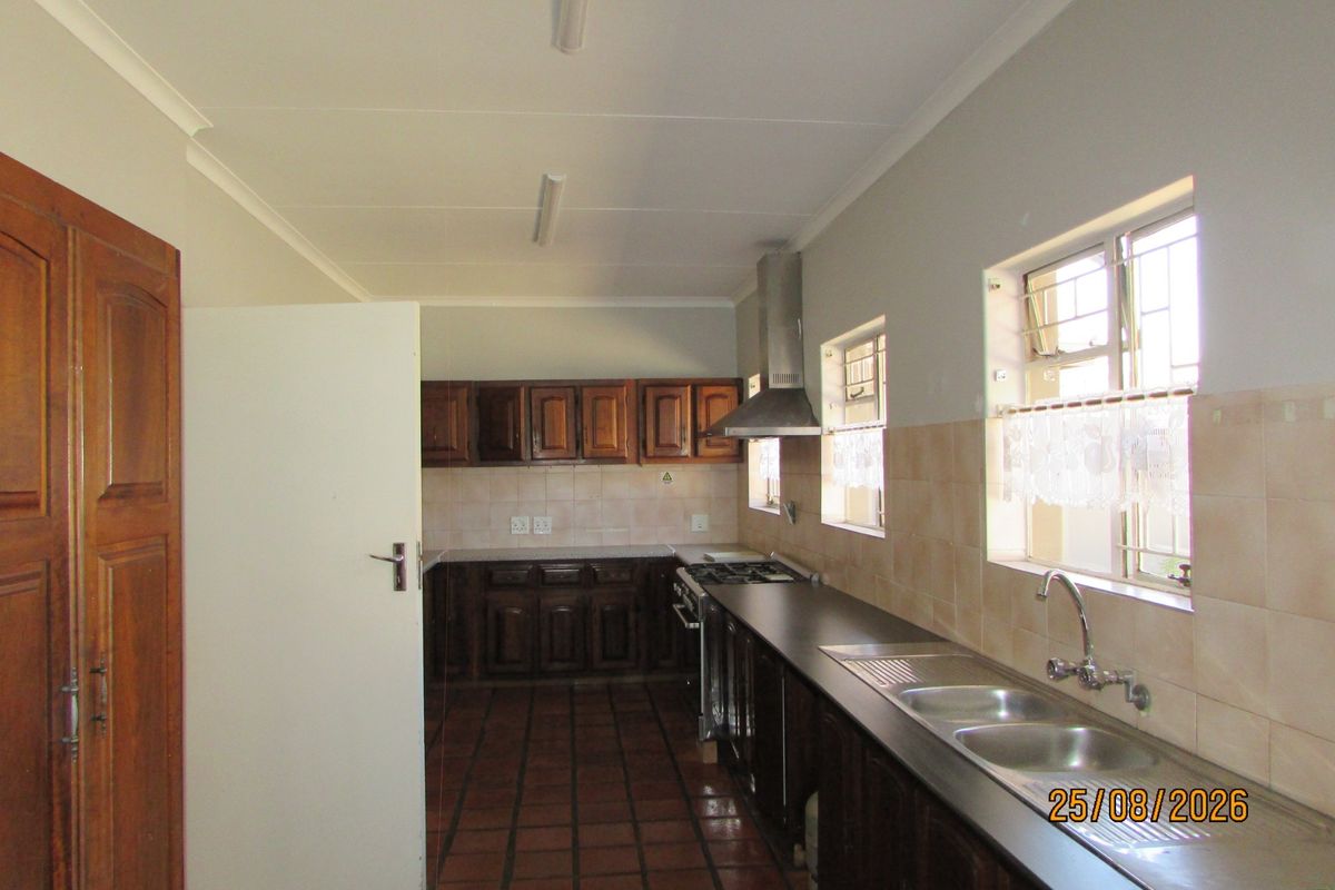 A functional kitchen featuring wooden cabinetry, a stainless steel sink, gas hob with extractor fan, and tiled flooring.