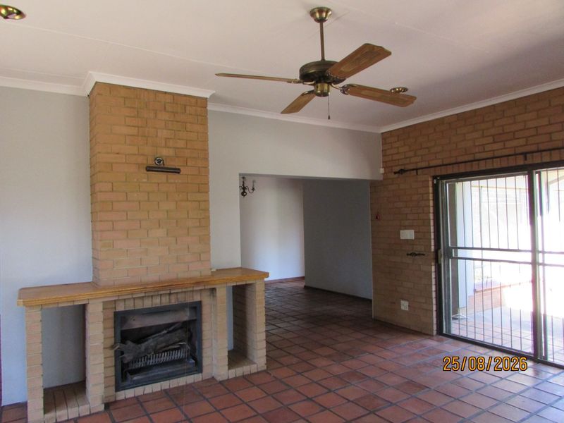Spacious living room featuring a prominent brick fireplace, terracotta floor tiles, ceiling fan, and sliding glass doors leading to the exterior.