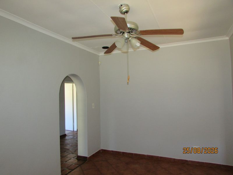 An empty living room featuring tiled flooring, a ceiling fan, and a distinctive arched doorway leading to an adjacent space.