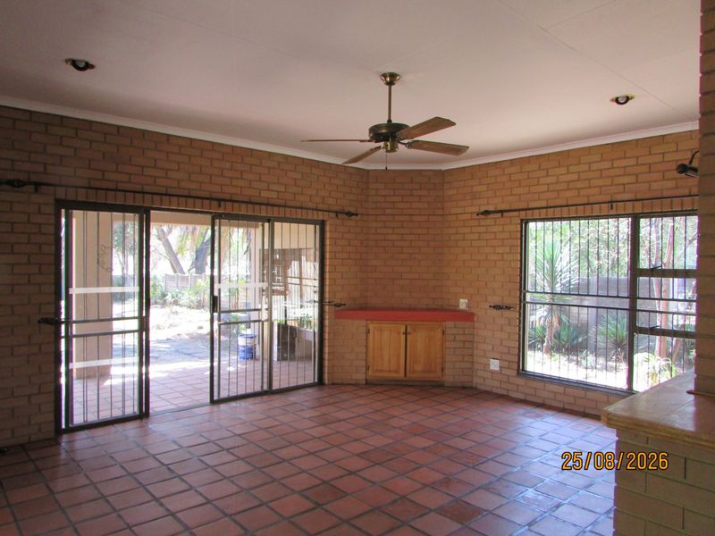 Spacious living area featuring exposed brick walls, terracotta floor tiles, ceiling fan, and sliding glass doors providing access to the outdoor patio.