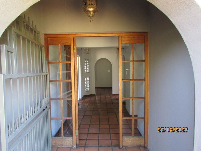 Entrance area featuring terracotta tiled flooring, timber-framed glass doors, and an arched entryway leading into the home interior.